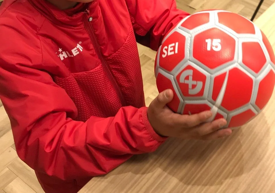 赤いジャケットを着た人物がサッカーボールを持っている様子