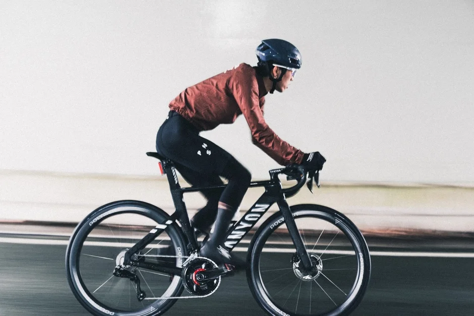 ヘルメットとサイクルウェアを着用した女性が、CANYONの黒いロードバイクに乗って走行している様子。