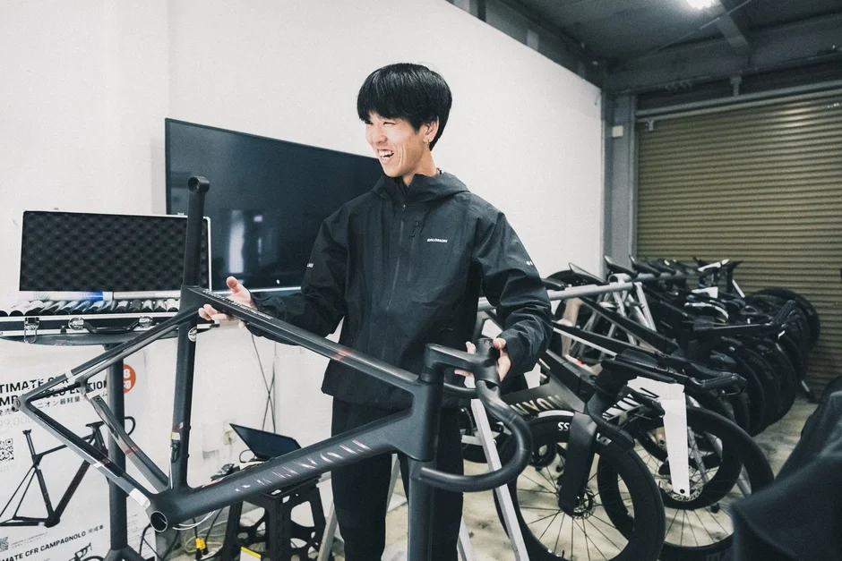 自転車のワークショップで、黒いロードバイクのフレームを持つ笑顔の男性。