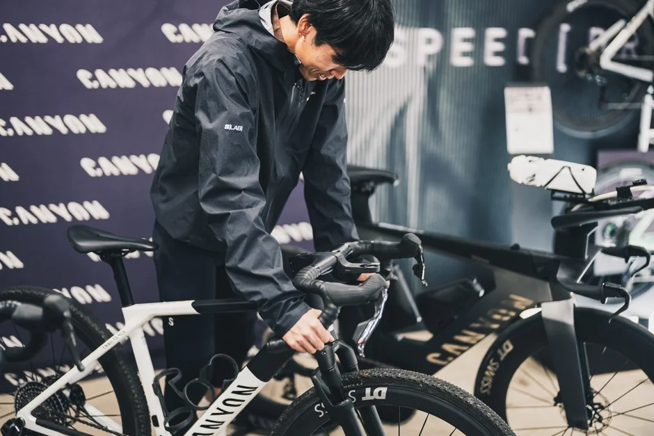 サイクリングウェアを着た男性が、CANYONのロゴが見える店内で白いグラベルロードバイクを調整している様子です。