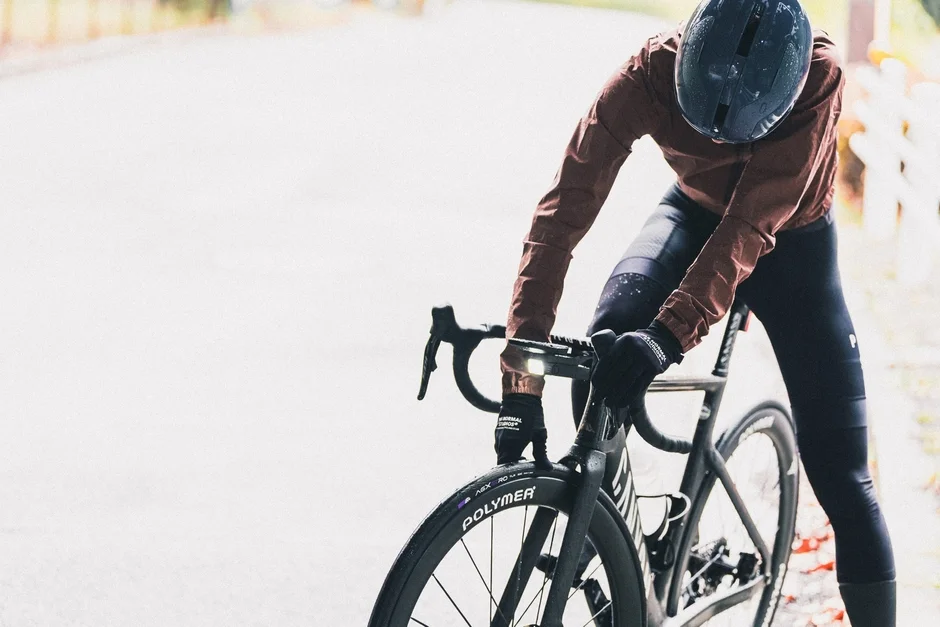 雨上がりの道でロードバイクに乗るサイクリストが、自転車に寄りかかって休憩している様子。