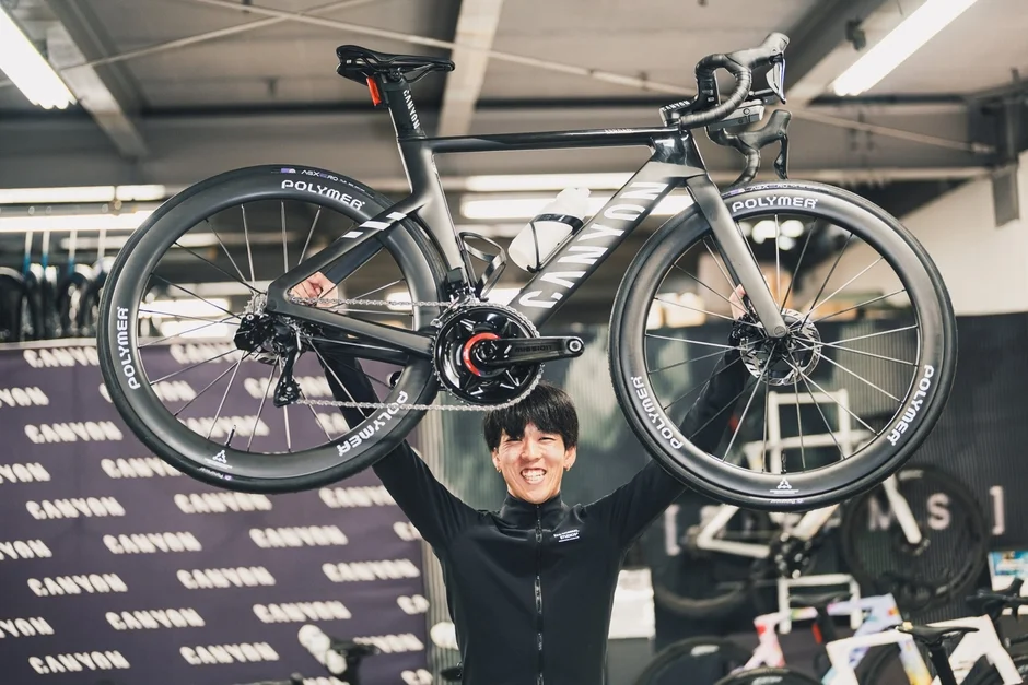 「CANYON」のロードバイクを頭上に掲げ、満面の笑みを浮かべる男性。
