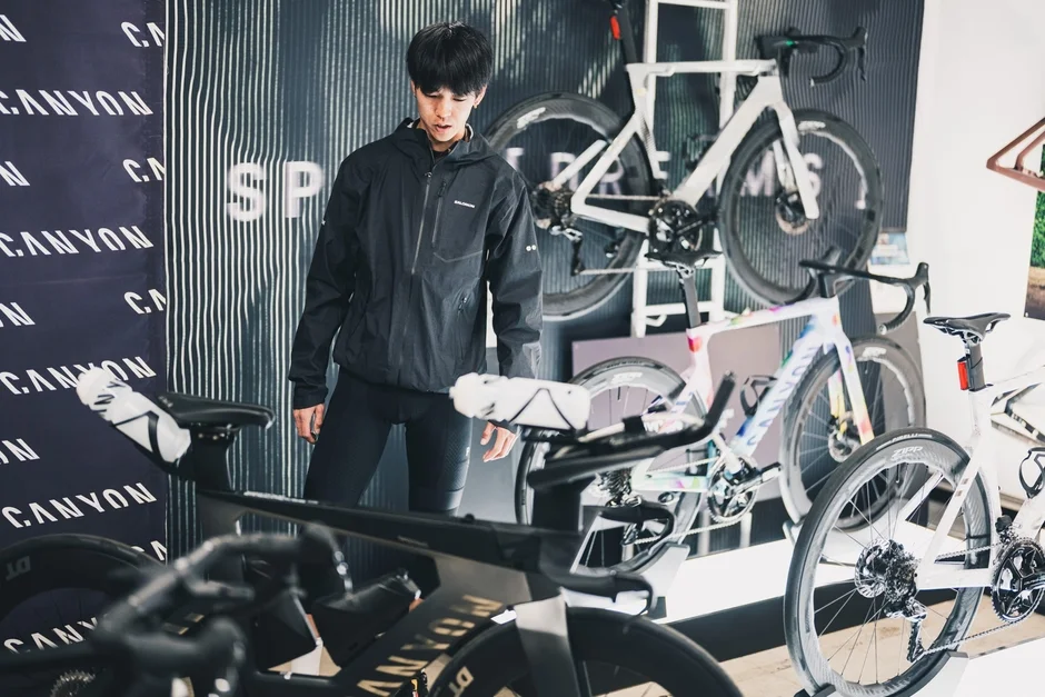 黒いジャケットを着た男性が、CANYONのロゴが入った高性能自転車が並ぶショールームで、自転車を眺めている様子です。
