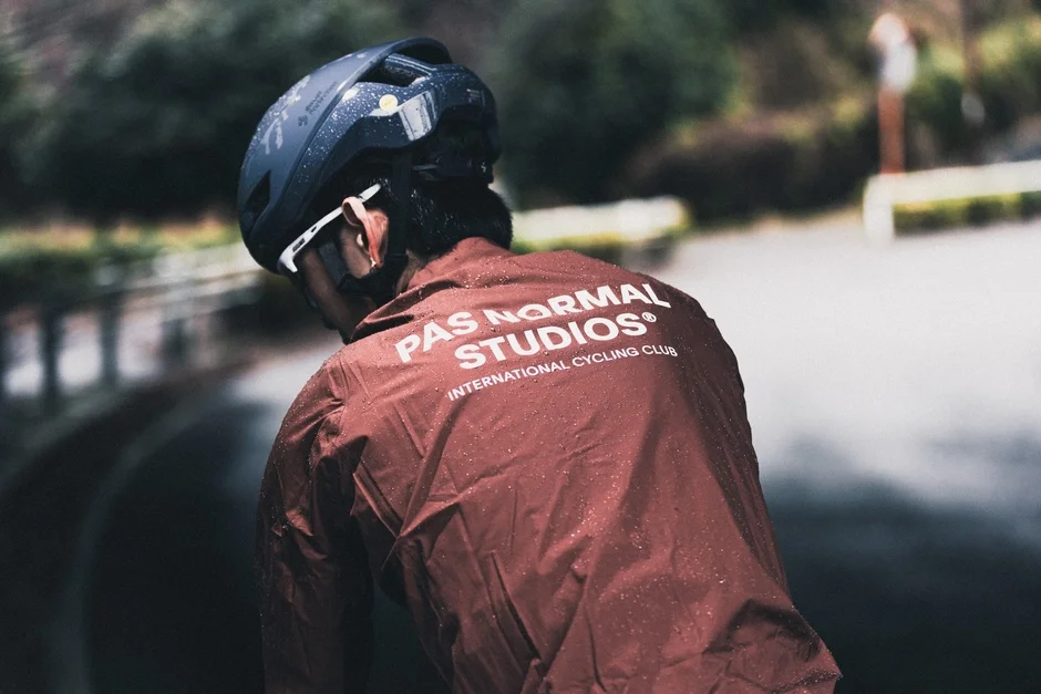 雨の中、サイクリング用ヘルメットと濡れたジャケットを着用した人物の後ろ姿。