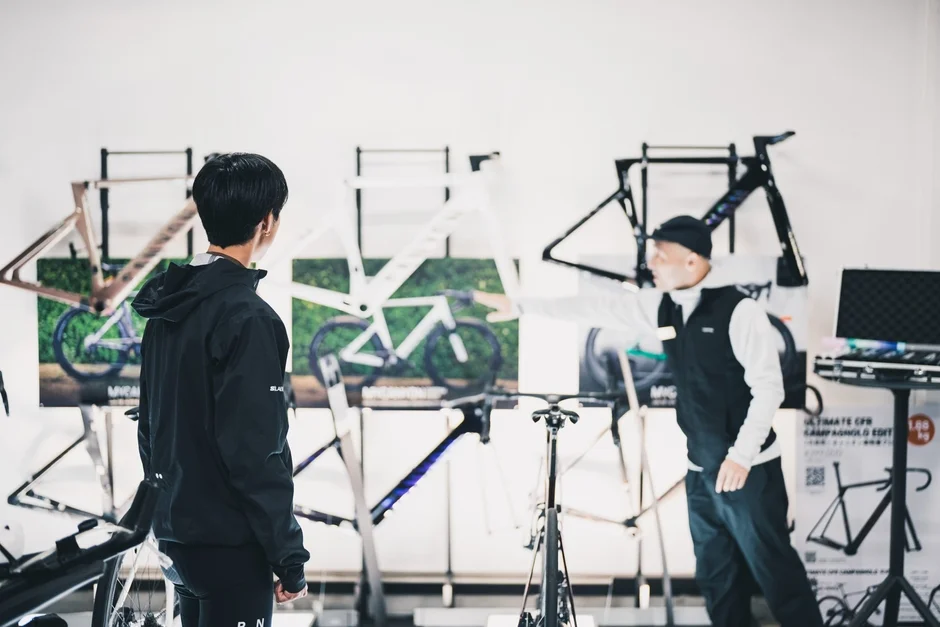 自転車のショールームで、店員らしき男性が顧客にロードバイクのフレームについて説明している様子。