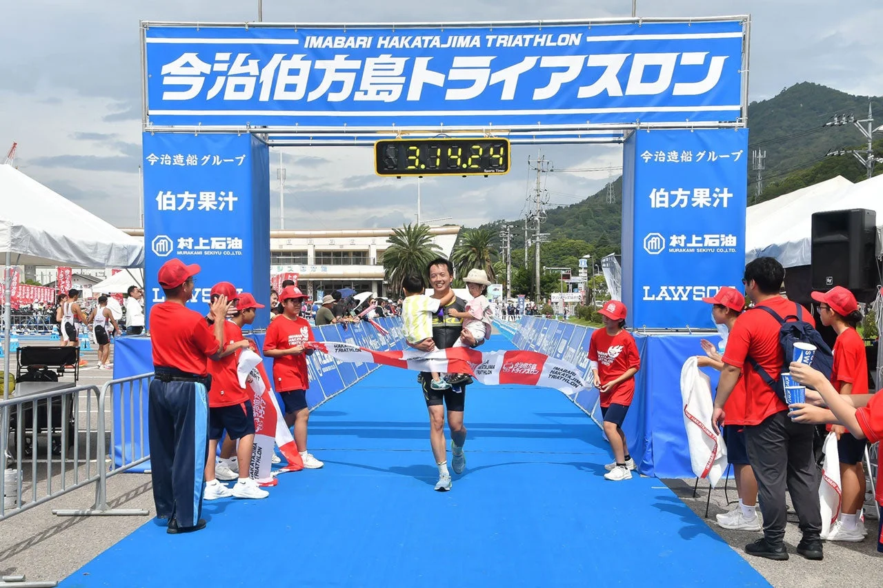 今治伯方島トライアスロンのゴール地点で子供たちを抱きかかえながら完走のテープを切る男性