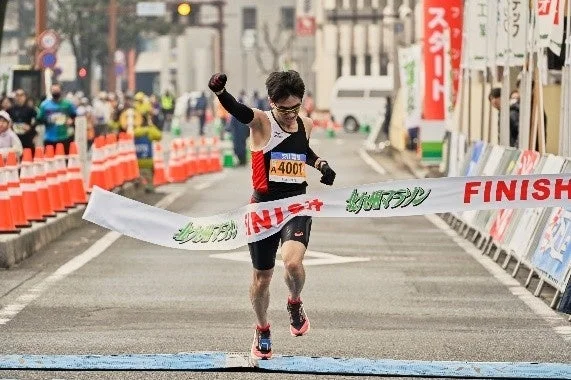 マラソン大会で、ゼッケンA4001のランナーがフィニッシュラインを力強く越え、右手を突き上げて喜びを表現している瞬間