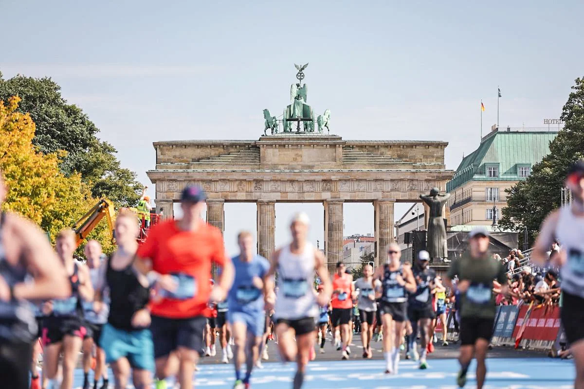 ベルリンのブランデンブルク門を背景に、多くのランナーが大規模なマラソン大会に参加している様子