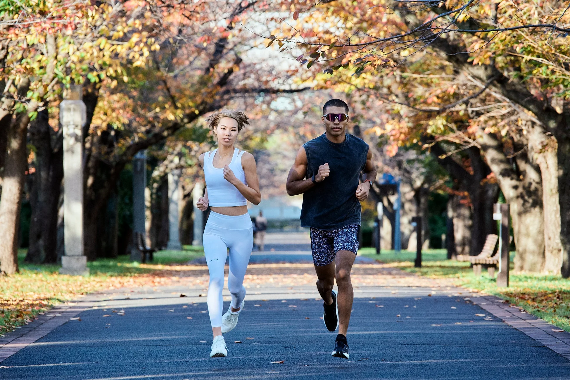 秋の並木道をジョギングする男女