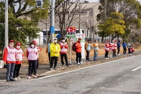 赤いベストを着た人々が道路脇に並び、何らかのイベントを応援している様子
