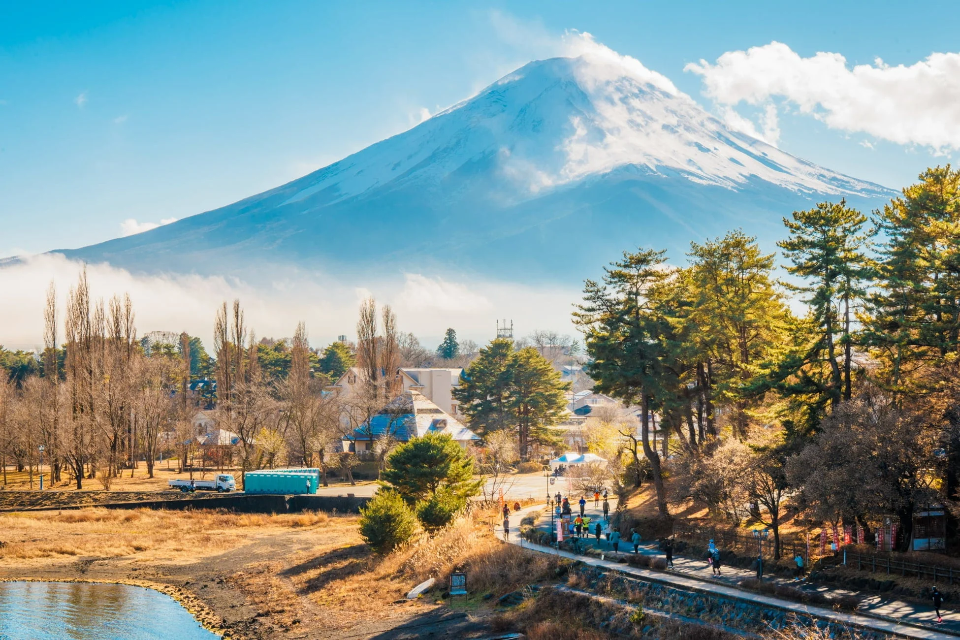 雪化粧した雄大な富士山を背景に、湖畔の散歩道で人々が散策やランニングを楽しむ冬の風景