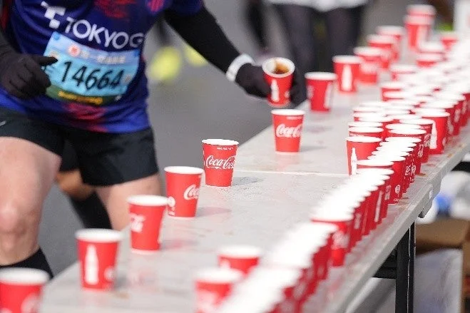 マラソン大会の給水所で、ランナーがコカ・コーラのカップを取ろうとしている様子